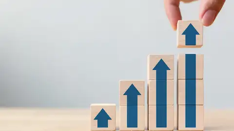 Uma mão adiciona um bloco de madeira com seta para cima a uma pilha crescente de blocos semelhantes.